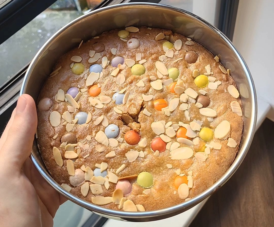 A photo of blondies in a cake tin with smarties and almond slices